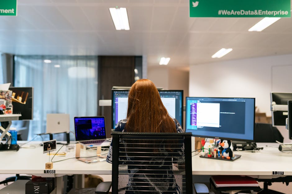 Back view of a female software engineer working at a multi-monitor setup in an office
